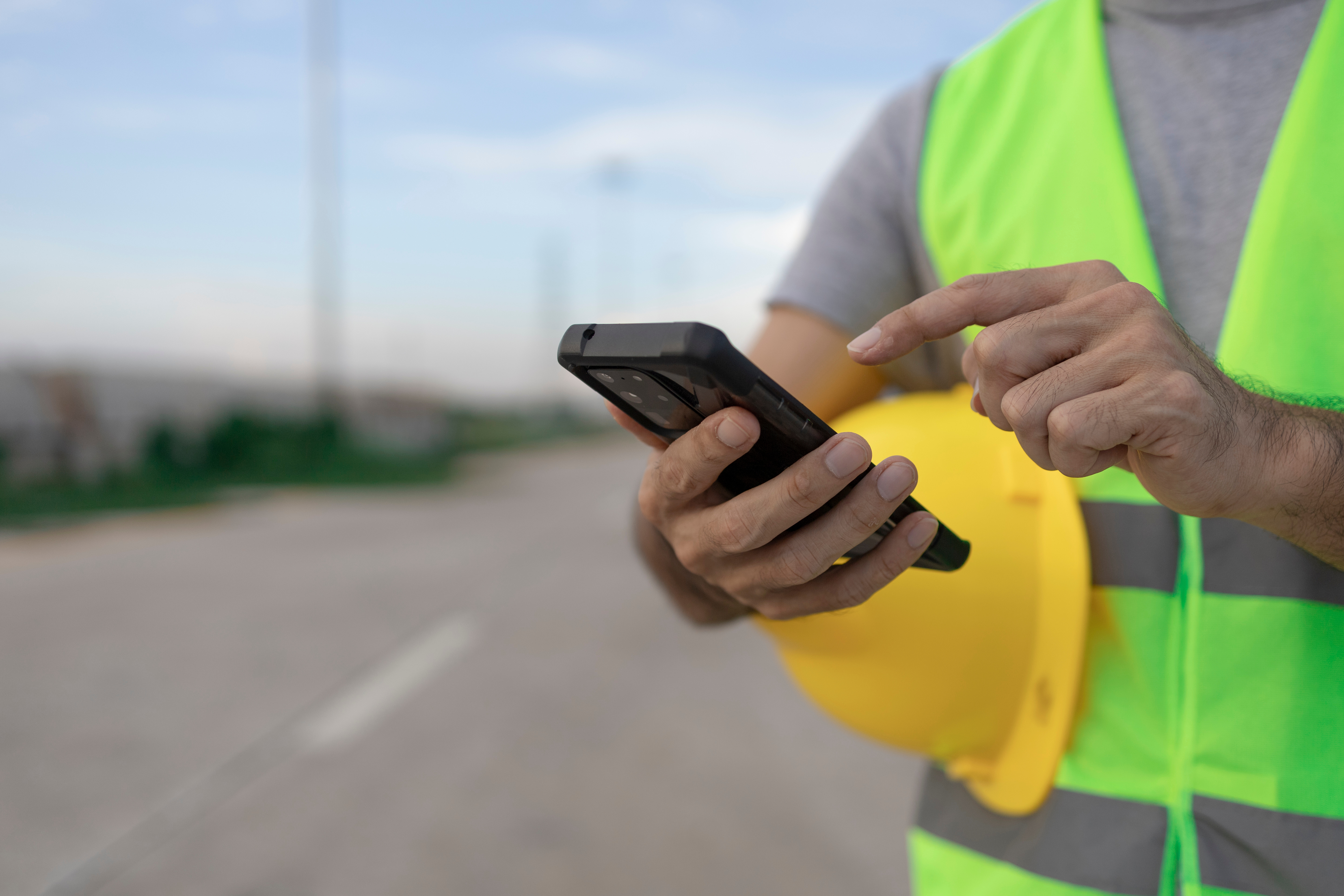 Worker in a hard hat using a smartphone outdoors at a construction site.