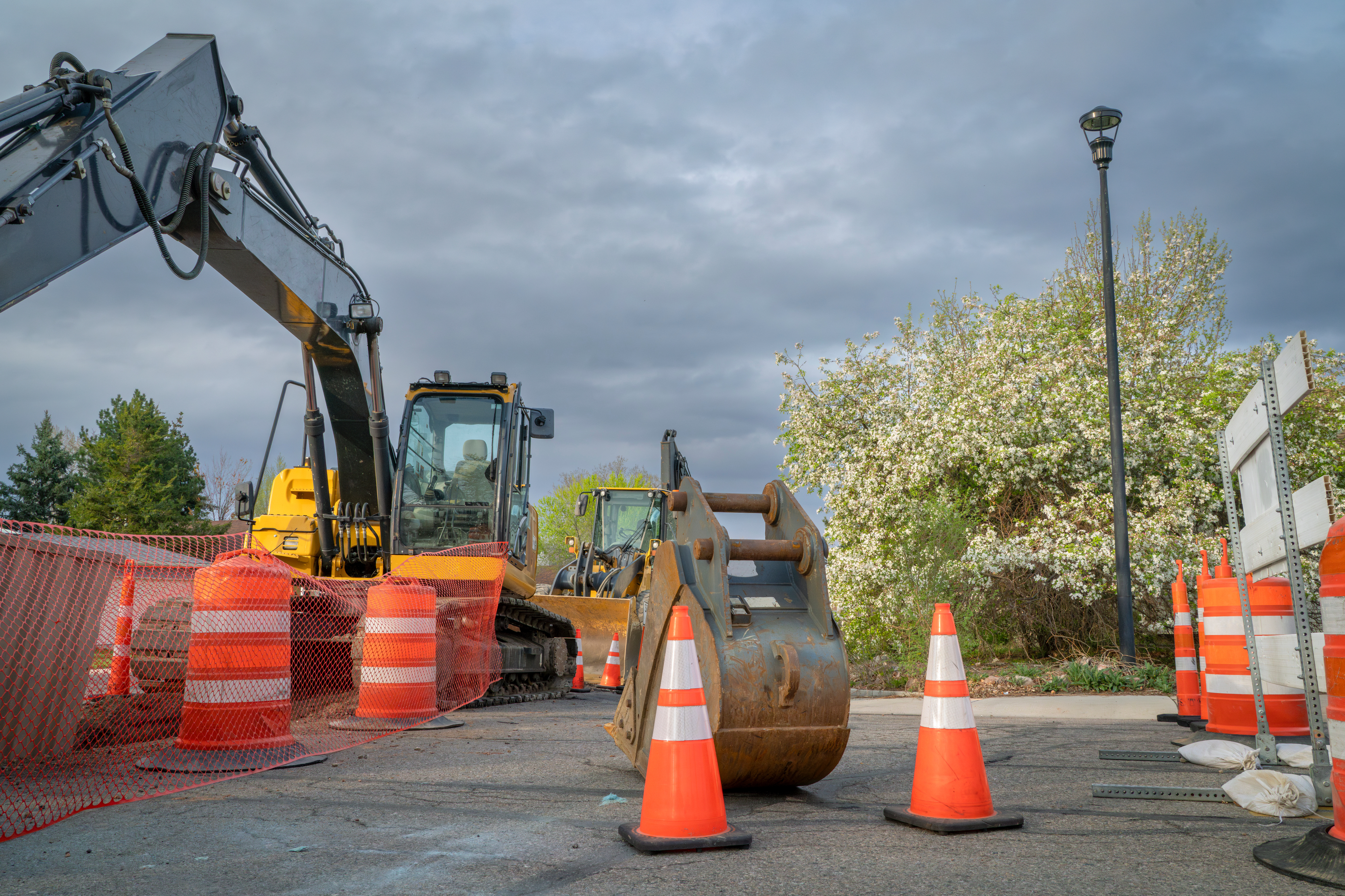 Road closed barrier blocking a residential street with heavy construction equipment in the background.
